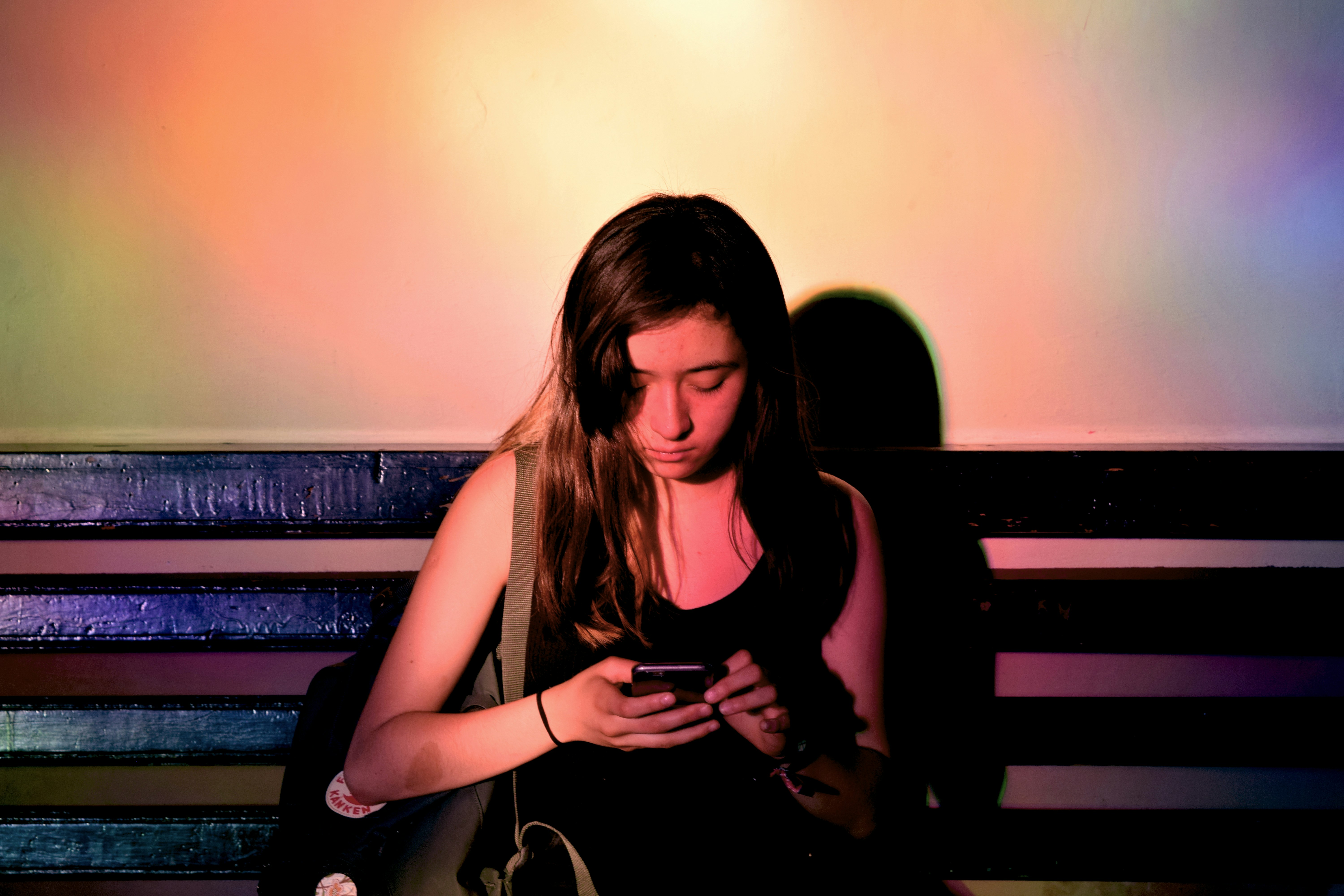 Person lit by colorful gradient light looking down at a smartphone