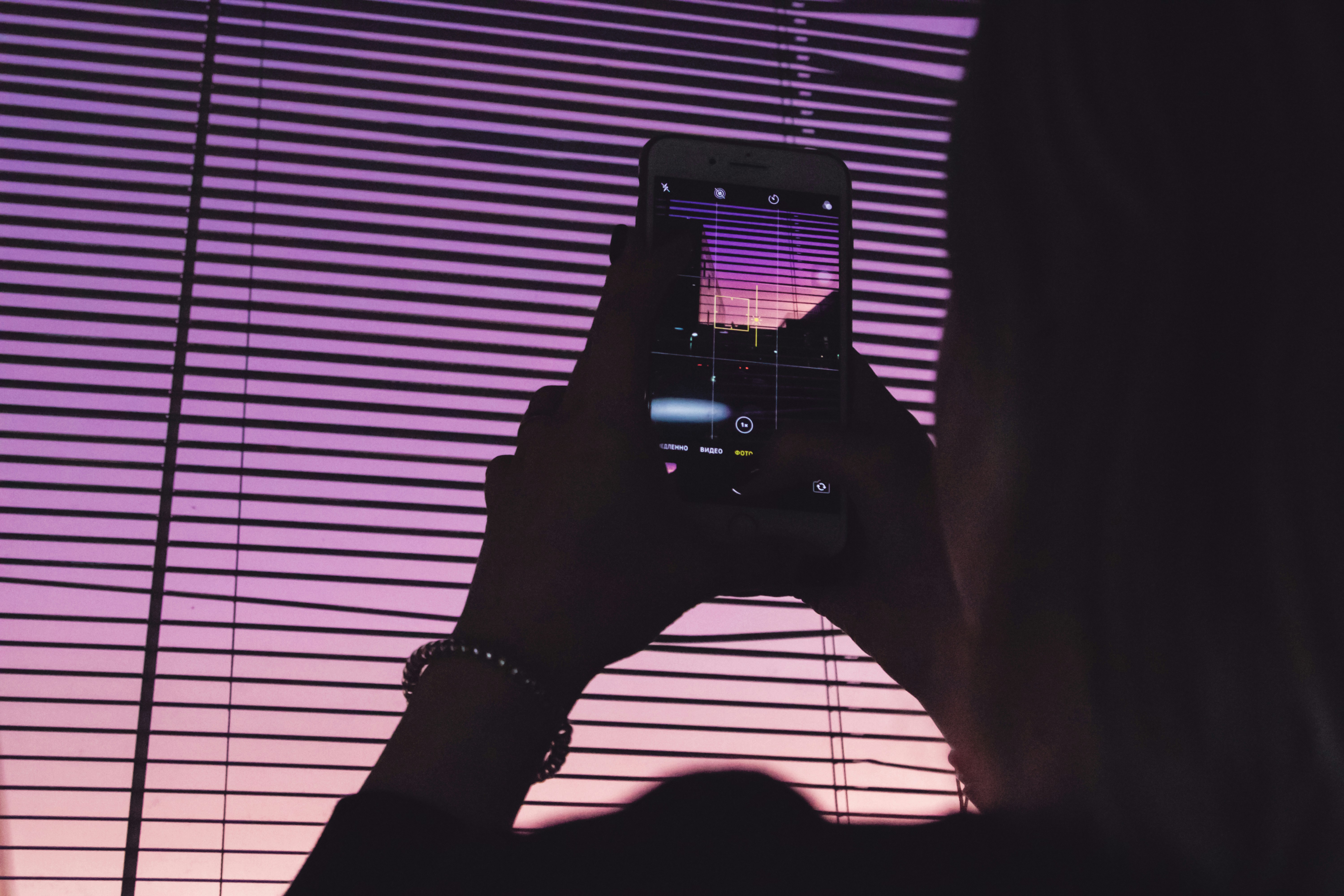 Silhouette holding a smartphone against purple window blinds